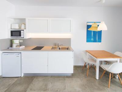 Kleine moderne Küche mit weißen Schränken, Holzarbeitsfläche, kleinem Kühlschrank und Essbereich mit zwei Stühlen.