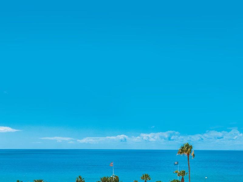Vista sulla costa con un hotel bianco e il mare blu sotto un cielo limpido.