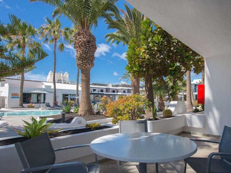 Terrazza con tavolo e sedie, vista su palme ed edifici moderni sotto il sole.