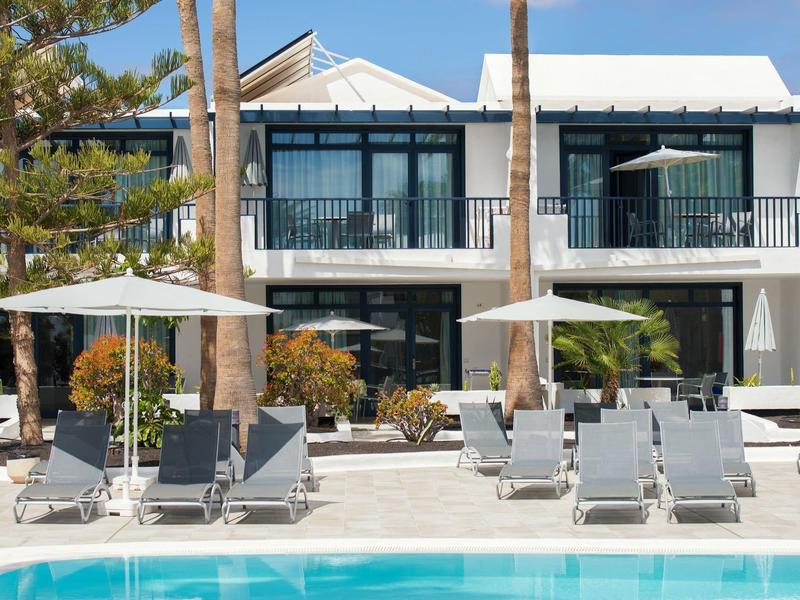 Area piscina moderna dell'hotel con lettini e ombrelloni bianchi sotto un cielo limpido