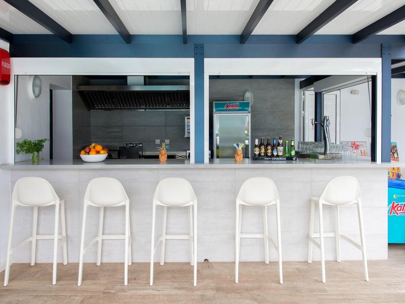 Area bar esterna moderna con cinque sgabelli bianchi davanti a un bancone e distributori di bevande.