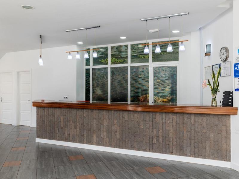 Area reception moderna di un hotel con grande bancone di legno e pareti bianche.