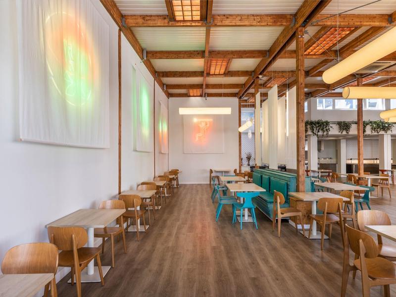 Sala da pranzo moderna con pavimenti in legno, tavoli, sedie e panche colorate.