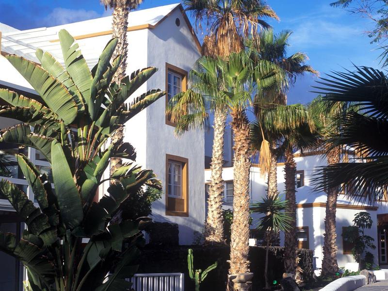 Edificio dell'hotel bianco con palme e piante tropicali sotto un cielo limpido.