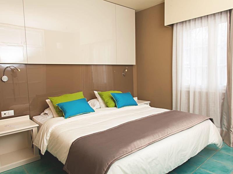 Camera d'hotel moderna con letto grande, cuscini colorati e comodini.