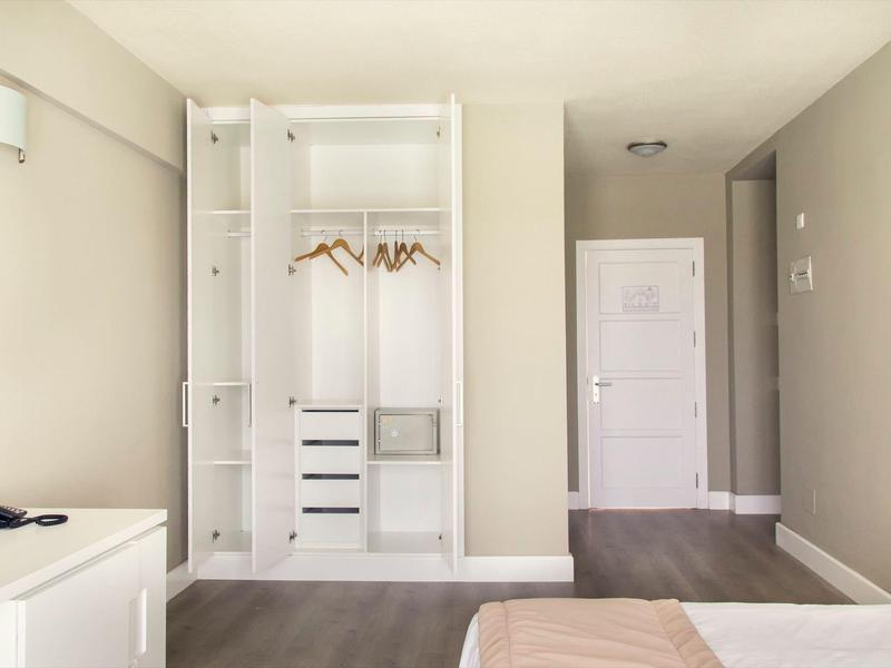 Camera d'albergo luminosa con armadio aperto, letto e porta sul corridoio.