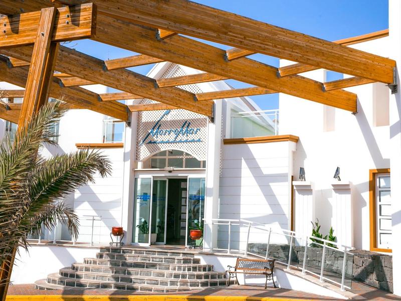 Ingresso dell'hotel con pergolato in legno, scale e porte scorrevoli in vetro con tempo soleggiato