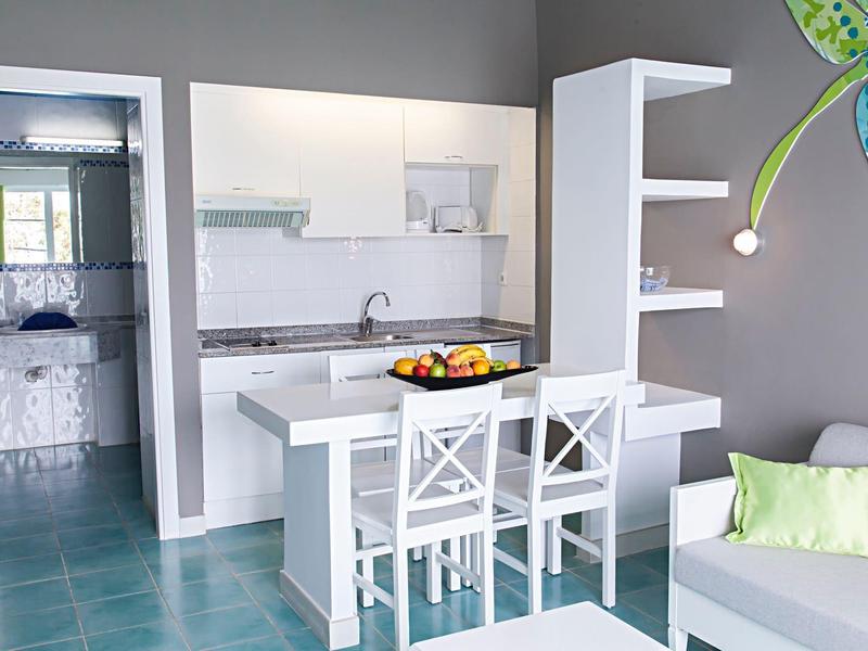 Area cucina moderna con piccolo tavolo, due sedie e ciotola di frutta decorativa nella camera d'hotel.