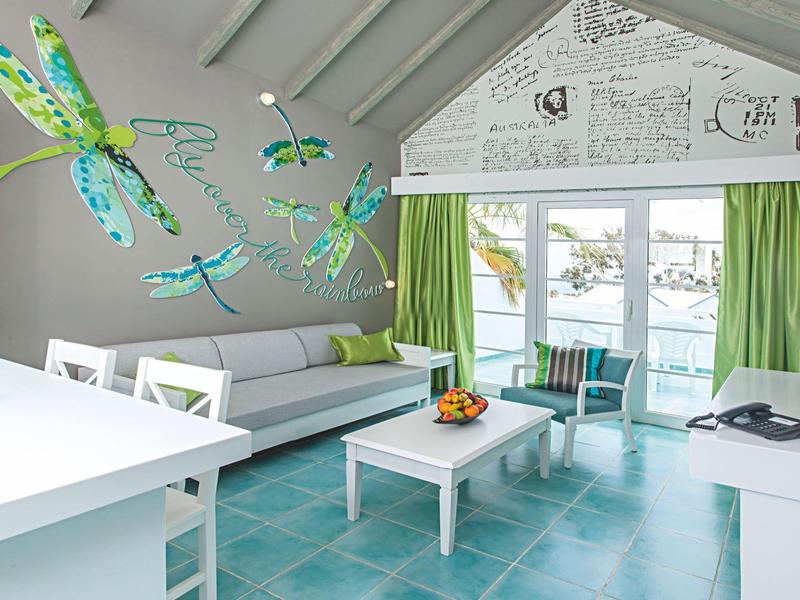 Soggiorno luminoso con piastrelle azzurre, mobili bianchi e tende verdi con vista sull'acqua