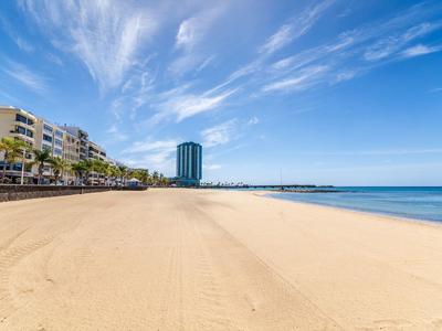 Ampia spiaggia sabbiosa vuota con edifici di hotel e cielo blu sullo sfondo.
