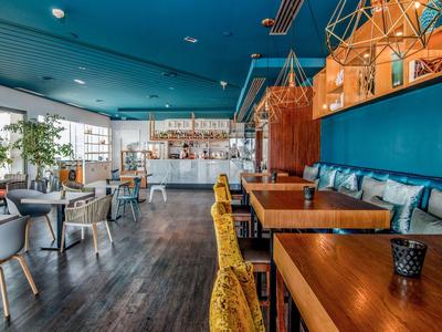 Area ristorante dell'hotel moderna con tavoli in legno, sedie gialle e decorazioni murali blu.