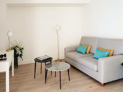 Soggiorno moderno con divano grigio, cuscini colorati e due tavoli piccoli su pavimento in legno.