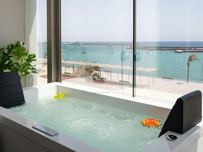 Vasca idromassaggio con vista sul mare e passeggiata, piante e petali di fiori decorano la vasca.