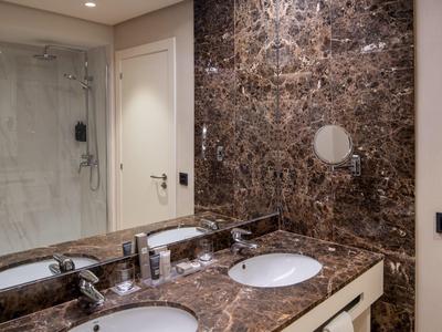 Bagno moderno con doppi lavandini e superfici in marmo accanto a una doccia.