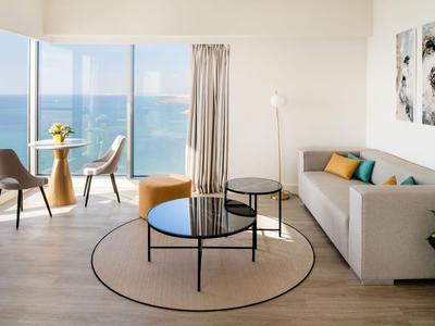 Soggiorno luminoso con vista mare, mobili moderni e porte scorrevoli in vetro che si affacciano sul balcone.