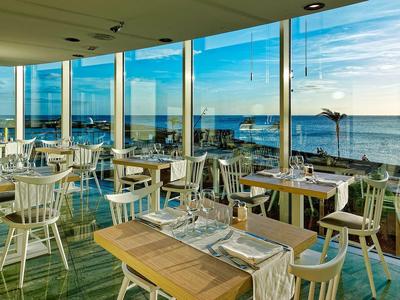 Ristorante luminoso con grandi finestre panoramiche che si affacciano sul mare al tramonto.