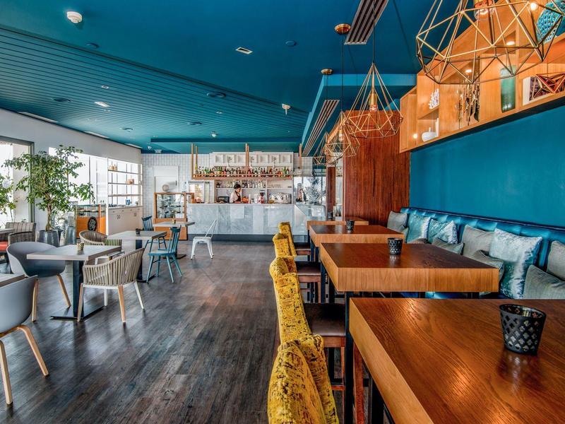 Ristorante d'hotel moderno con tavoli in legno, sedie colorate e luci decorative al soffitto.