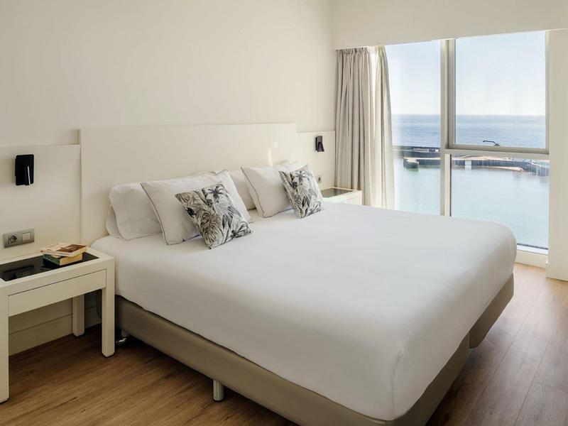 Camera d'hotel moderna con letto grande, comodino e vista sul mare da grandi finestre