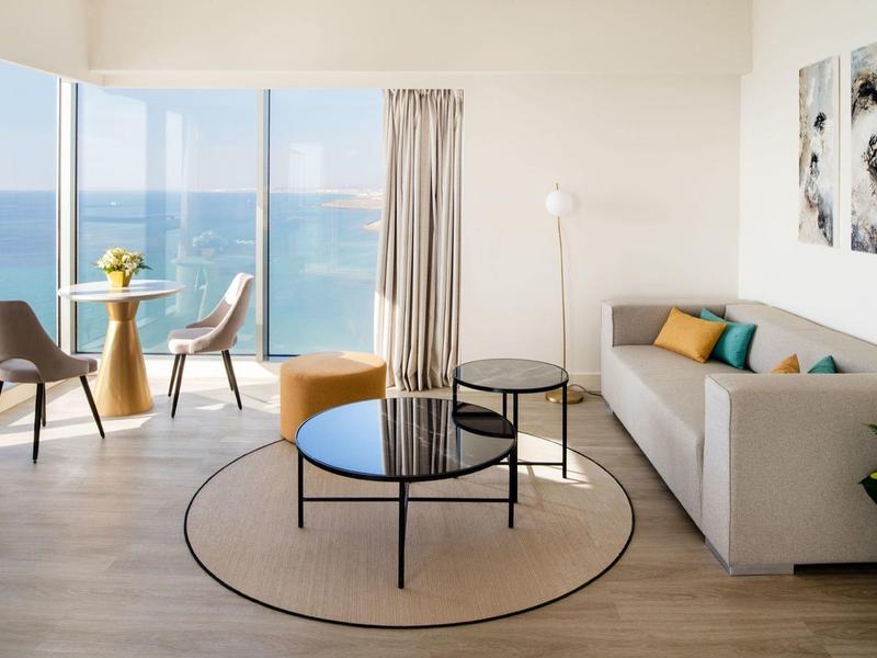 Soggiorno luminoso con vista mare, mobili moderni e porte scorrevoli in vetro che si affacciano sul balcone.