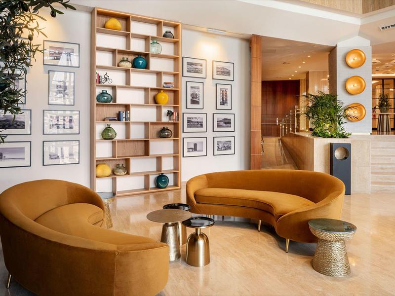 Area d'attesa elegante con divani marroni, scaffali progettati e illuminazione calda.