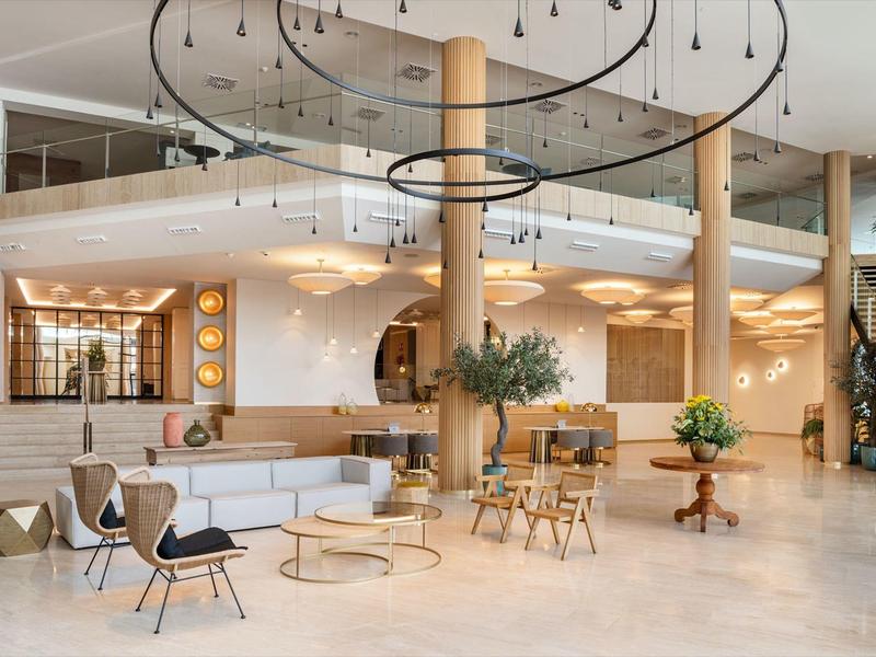 Area lounge moderna dell'hotel con sedie, tavoli, piante e illuminazione a soffitto a spirale.