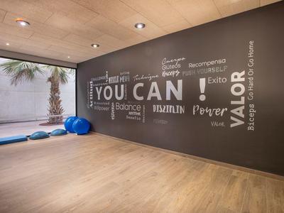 Moderner Fitnessraum mit Holzboden, dunkler Wand mit motivierendem Text und bunten Gymnastikbällen.