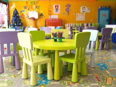Buntes Klassenzimmer mit kleinen grünen und lila Tischen und Stühlen auf gemusterter Bodentapete.