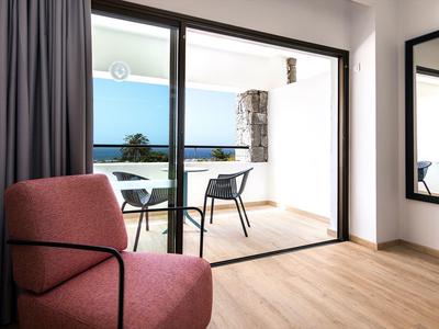 Moderner Raum mit Holzfußboden, rotem Sessel, großem Spiegel und Balkon mit Blick aufs Meer.
