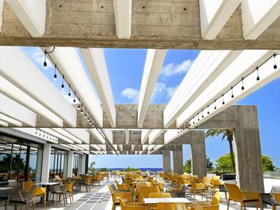 Modernes Hotelrestaurant mit gelben Stühlen und Blick auf den Strand unter blauem Himmel.