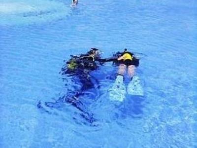 Zwei Taucher schwimmen im klaren blauen Poolwasser mit Flossen und Tauchausrüstung.