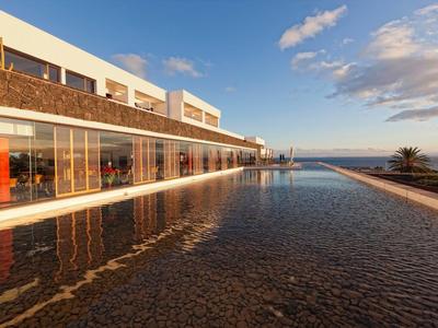 Moderner Bau mit Glasfront und flachem Wasserbecken bei klarem Himmel am Meer.