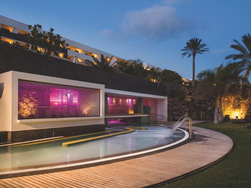 Edificio moderno di un hotel con finestre illuminate accanto a una piscina al crepuscolo.