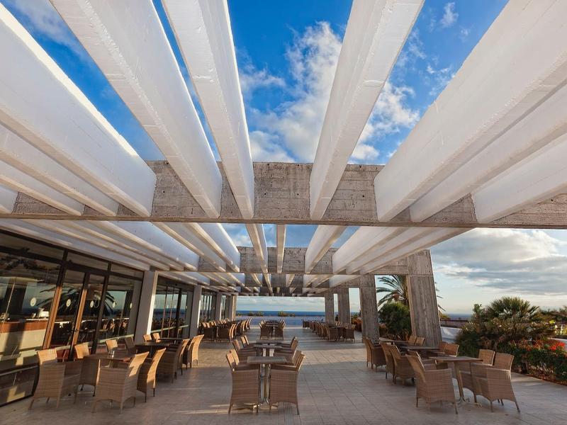 Balcone aperto con sedie e tavoli in legno sotto pergola bianca con vista mare
