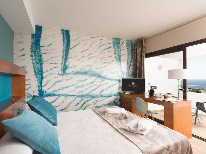 Camera d'hotel moderna con letto, scrivania e balcone con vista mare.