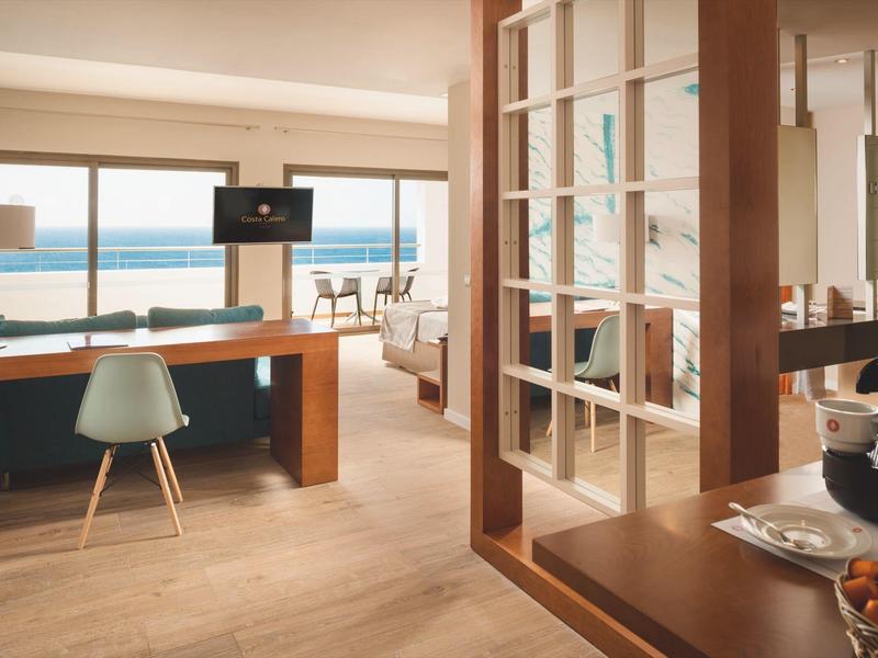 Camera d'hotel luminosa con scrivania, area salotto e vista sul mare.