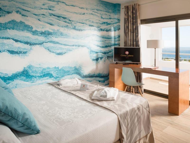 Camera d'hotel moderna con vista mare, scrivania e letto con cuscino blu.