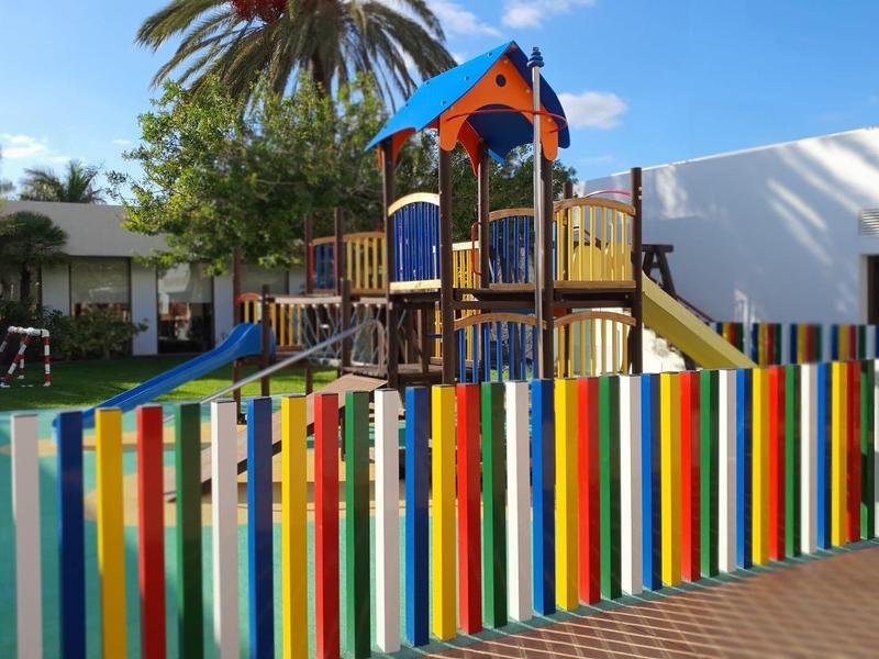 Area gioco colorata con scivolo e recinzione multicolore all'esterno di un edificio bianco.