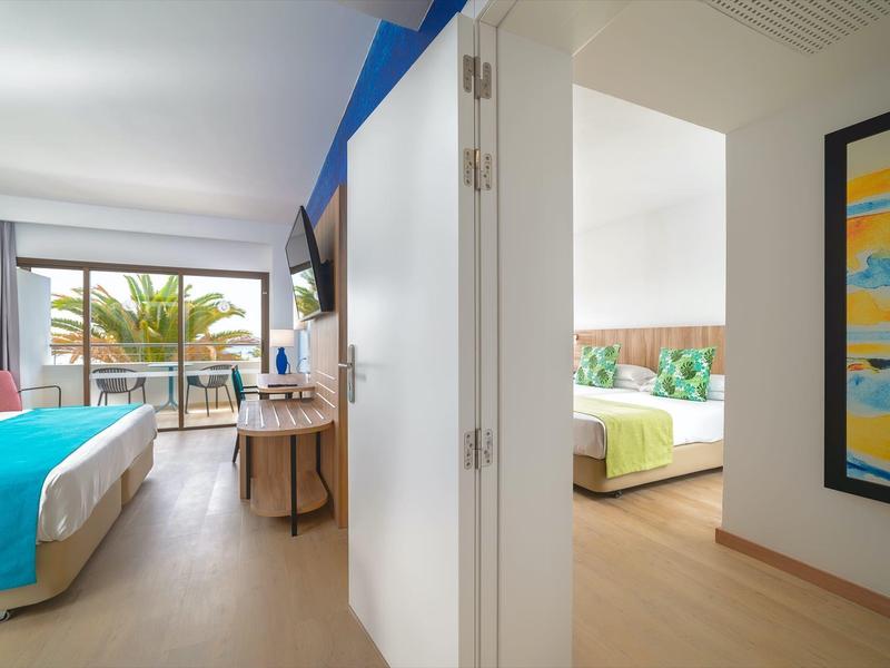 Camere d'hotel luminose con arredi moderni, balcone e vista sulle palme.