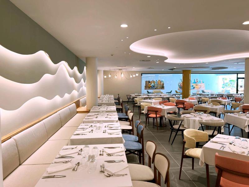 Area ristorante moderna con tavoli bianchi e illuminazione decorativa a parete.