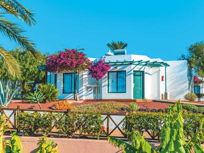 Weißes Ferienhaus mit blühenden Pflanzen und blauer Himmel im Hintergrund.