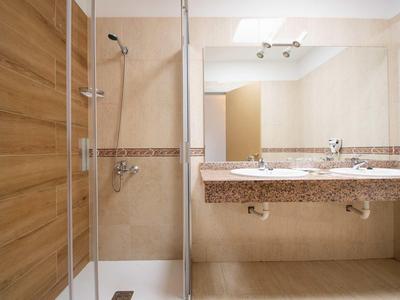 Moderner Badezimmer mit Dusche, Holz- und Beige-Fliesen, zweifachem Waschbecken und großem Spiegel.