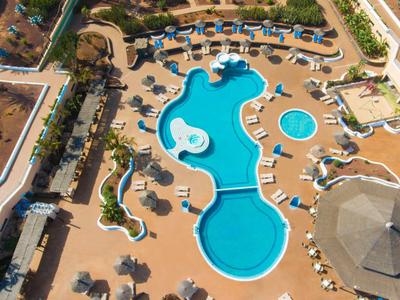 Luftaufnahme eines großen, geschwungenen Pools mit Sonnenschirmen und Liegestühlen im Hotelbereich.