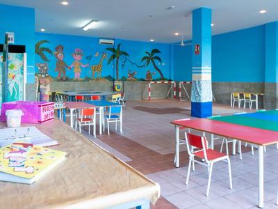 Bunter Spielraum mit Tischtennisplatte, Sitzgruppen, Wandmalerei und Spieltischen in hellblauem Raum.