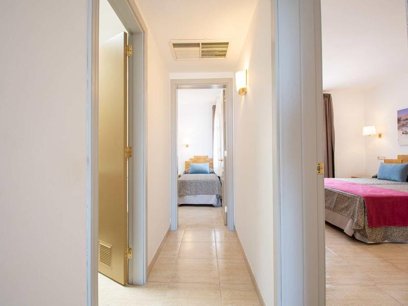 Heller Flur mit beige Fliesen, links offene Tür, beleuchtete Räume am Ende und rechts Schlafzimmer.