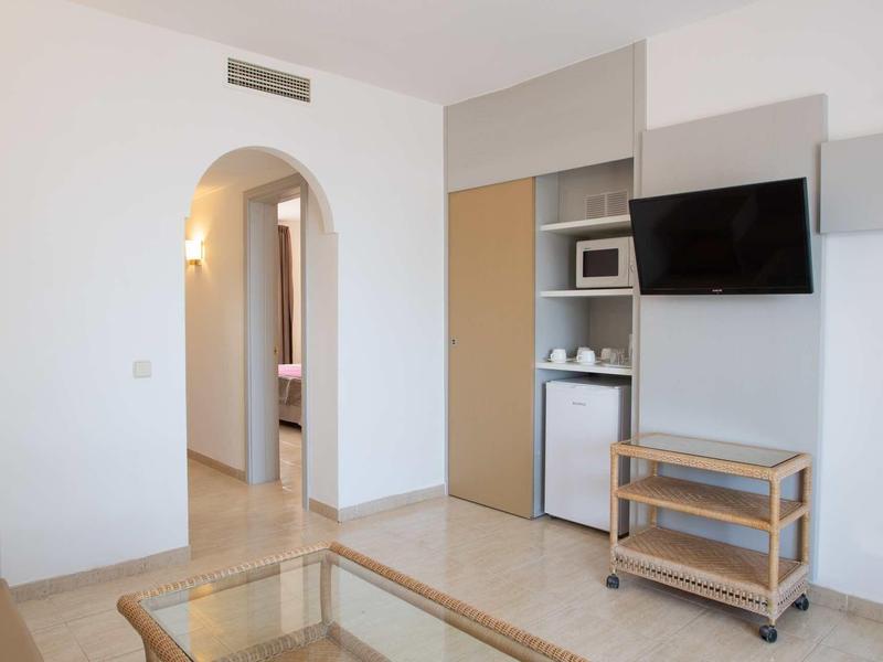 Minimalistischer Raum mit weißem Wandanstrich, Fernseher, Mikrowelle, kleinem Kühlschrank und Holzwagen.