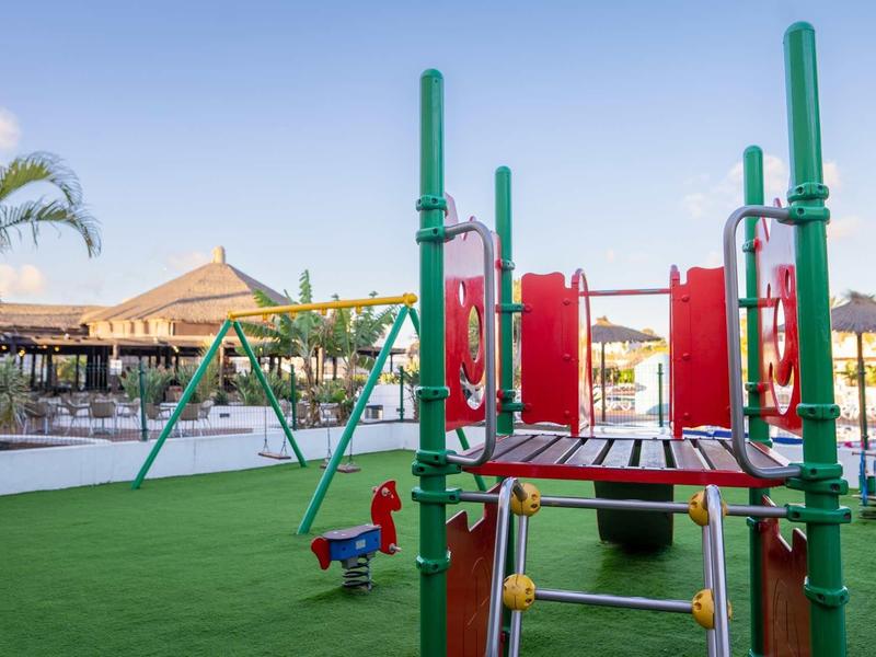 Bunter Kinderspielplatz mit Rutsche und Federwippe auf grünem Kunstrasen im sonnigen Freizeitpark.