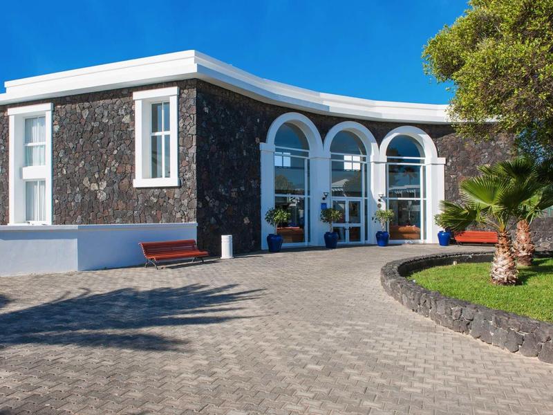 Hotelentree met donkere stenen gevel en drie grote gebogen ramen.