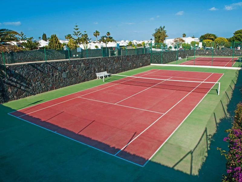 Rood tennisveld met groene randen en witte lijnen onder een blauwe lucht.