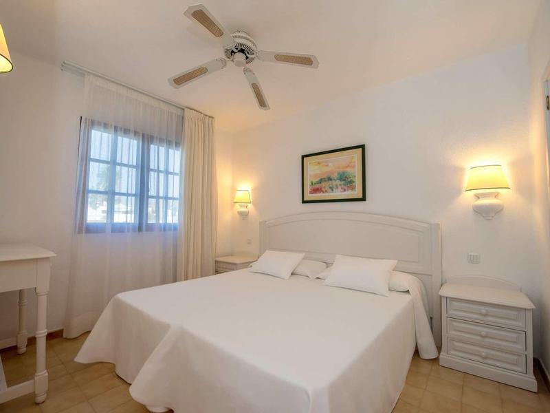 Licht, eenvoudig ingericht hotelkamer met tweepersoonsbed, plafondventilator en nachtkastjes.