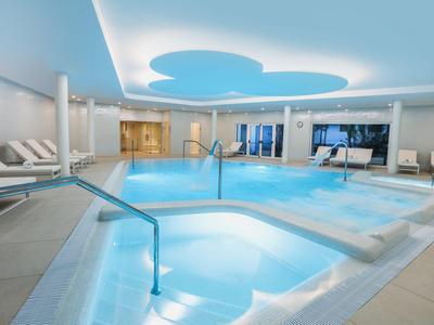 Beleuchteter Innenpool und Whirlpool mit Liegestühlen in einem modernen Hotel-Spa.